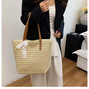 Detail of hand-woven straw tote bag with white lace bow and brown leather strap