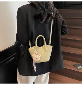 Détail d'un sac seau en cuir vert avocat avec breloque ours sur une tenue blazer noir