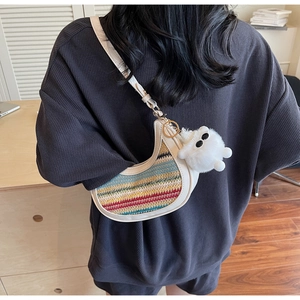 Detail of colorful striped crescent bag with a white plush monster charm on shoulder