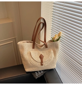 Detail of woven straw tote bag with brown faux leather straps and front pocket