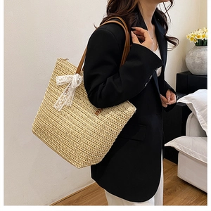 Detail of hand-woven straw tote bag featuring a large white lace bow and brown leather straps