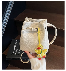 Detail view of white lychee textured bucket bag with a cute yellow duck pendant on dark wood