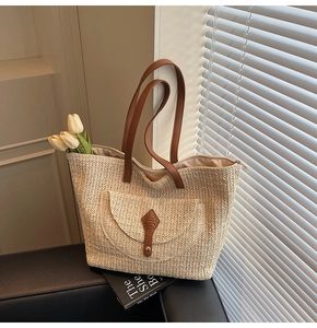 Detail of a large straw tote bag featuring brown faux leather straps and front pocket