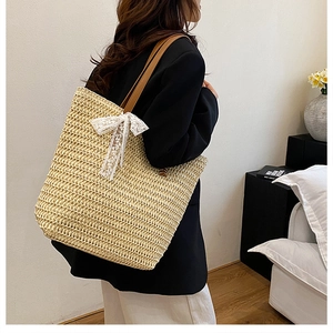 Detail view of large straw tote bag with brown leather straps and white lace bow decoration