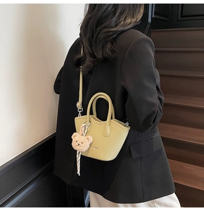 Détail du sac seau en cuir vert pistache avec un charmant petit ours en peluche beige