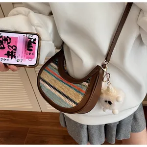 Detail of bohemian striped woven crescent bag with brown strap and plush monster charm