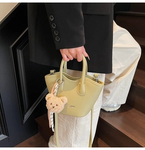 Détail d'un sac seau vert clair en cuir grainé avec foulard en soie et breloque ours