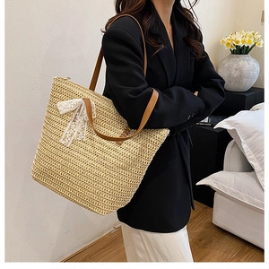 Detail of woven straw tote bag featuring white lace bow and brown leather shoulder strap