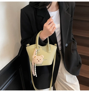 Détail du mini sac seau vert clair avec pendentif ours et texte de mode sur le cuir