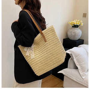 Straw tote bag detail with white lace bow and brown leather strap on model