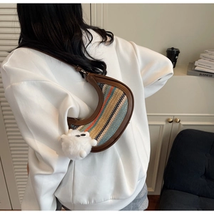 Detail of multi-color striped woven half-moon bag with brown strap and pompom charm