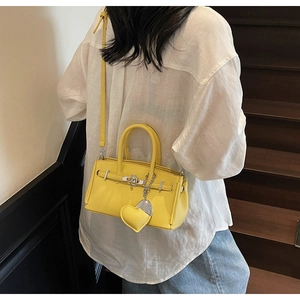Dettaglio di una borsa a mano gialla in pelle con motivo litchi e tracolla indossata da modella