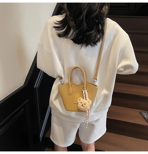 Mini sac seau jaune à motif litchi avec breloque ours porté sur une tenue blanche