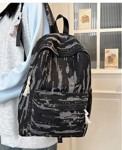 Detailed side view of denim striped backpack featuring white tassel zippers and large pockets