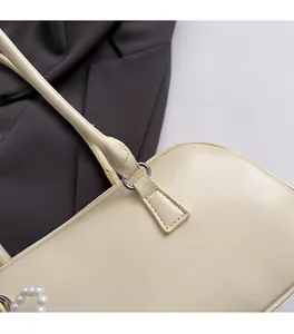 Dettaglio della fibbia in metallo dorato e ciondolo di perle su borsa in pelle beige