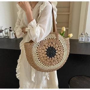 Detail of a large round woven straw shoulder bag with a sunburst pattern and brown leather straps