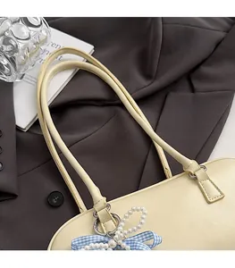 Dettaglio borsa crema in pelle con cinturino di perle e fiocco a scacchi blu