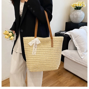 Detail of cream straw tote bag featuring brown leather straps and white lace bow decoration