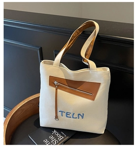 Détail du sac en toile beige avec poche en cuir marron et broderie TELN bleue