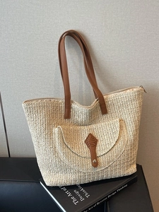 Large beige woven straw tote bag with brown leather handles and decorative front pocket