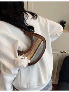 Striped woven hobo bag with brown leather trim and fluffy charm on a female model