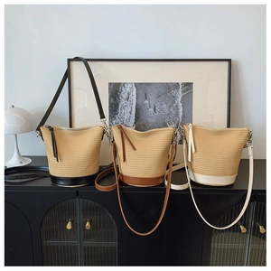 Three woven straw bucket bags in black, brown, and cream displayed on a sleek black cabinet