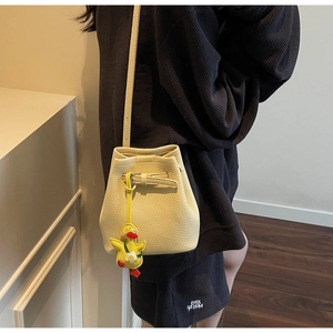 Close-up of beige bucket bag in lychee texture with a cute yellow duck charm detail