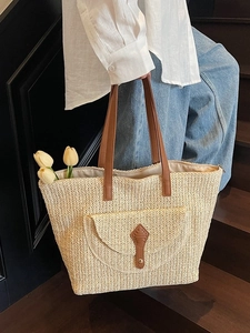 Large beige woven straw tote bag with brown leather handles and front pocket detail