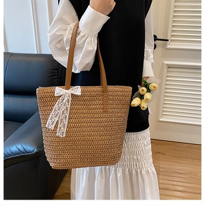 Detailed close-up of woven straw tote bag with white lace bow and leather straps