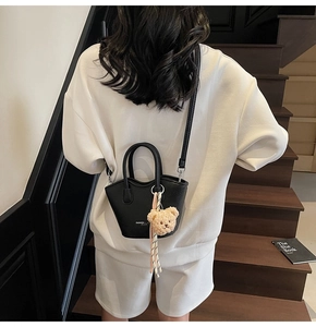 Détail d'un mini sac seau noir en cuir avec un charmant pendentif d'ours en peluche