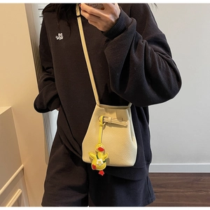 Model wearing a cream-white litchi grain bucket bag with a yellow duck charm