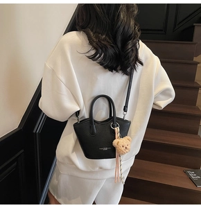 Détail d'un sac seau en cuir grainé noir avec charme d'ours porté par un mannequin