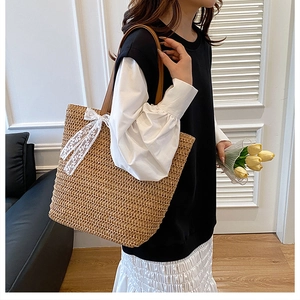 Detail of a large straw tote bag featuring white lace bow and brown leather shoulder straps