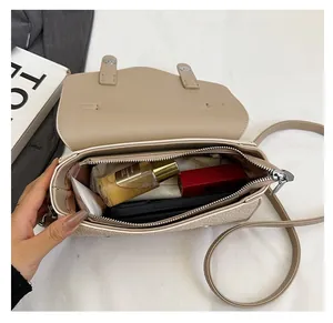 Detail view of the spacious inner compartment and zipper pocket of this beige crossbody bag