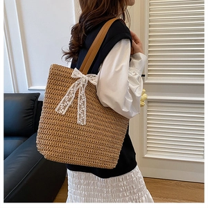 Close-up of woven straw tote bag with a white lace bow detail and brown leather straps