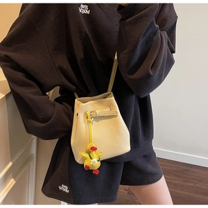 Detail view of beige lychee leather bucket bag with cute yellow duck pendant decoration