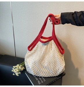 Detail van rood gebreid handvat en merklabel op de witte geweven mesh draagtas