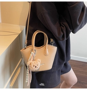 Détail du sac seau beige avec texture litchi, breloque ours en peluche et bandoulière