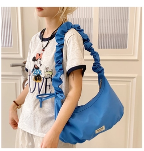 Details der blauen plissierten Halbmondtasche mit breitem Gurt und Markenemblem