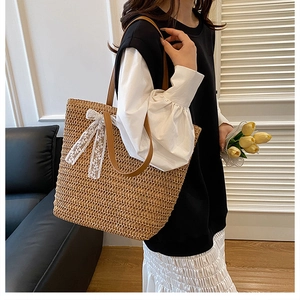 Detail of hand-woven straw tote bag with white lace bow and brown leather shoulder strap