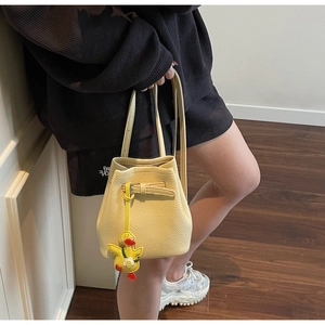 Detailed shot of yellow lychee leather bucket bag with cute duck charm and drawstring closure