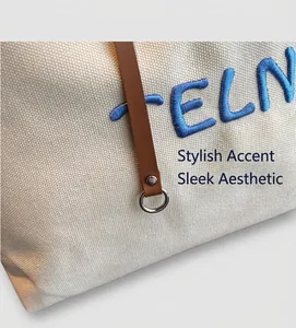 Détail du sac en toile beige avec broderie bleue, bandoulière en cuir et rivets