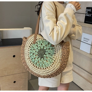 Detail of handwoven round straw beach bag showing green contrast stitching and leather straps