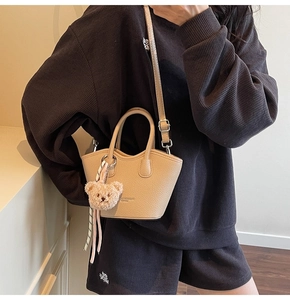 Vue latérale du sac seau beige avec charme d'ours en peluche et cuir grainé