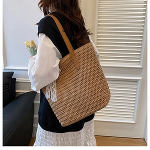Detail of hand-woven straw tote with brown leather strap and delicate lace bow accent