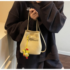 Detail of beige litchi grain leather bucket bag with cute yellow duckling charm