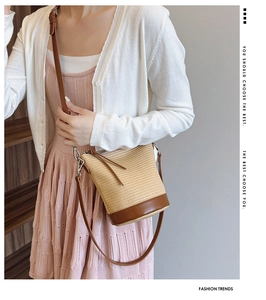 Detail of straw woven bucket bag with brown leather trim and zipper closure on a model