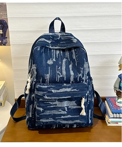 Detail of vintage denim backpack with white tie-dye patterns and woven tassel zipper pull