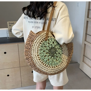 Detail of round straw tote bag featuring green and beige woven patterns and leather straps