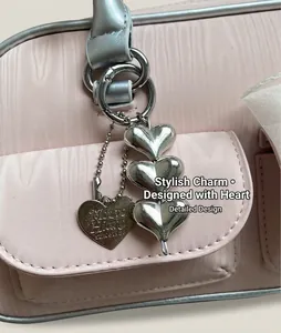 Detail of silver triple heart metallic charms with engraved logo on a pink bag